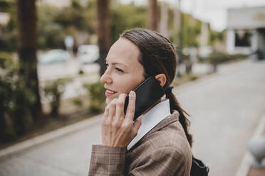 Lächelnde weibliche Fachkraft, die mit einem Mobiltelefon spricht und dabei wegschaut - DMGF00487