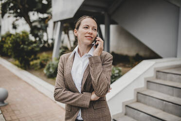 Businesswoman talking on smart phone while standing against building - DMGF00488