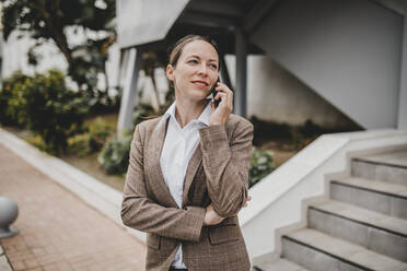 Geschäftsfrau, die mit einem Smartphone telefoniert, während sie vor einem Gebäude steht - DMGF00488