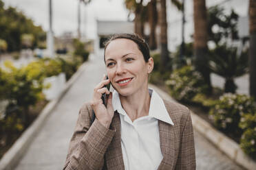 Smiling female entrepreneur talking on phone looking away - DMGF00489