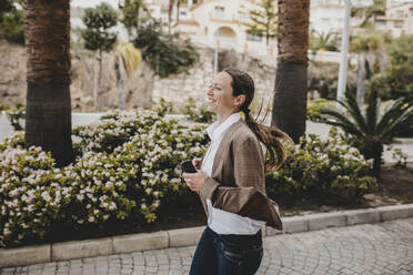 Fröhliche Frau mit Smartphone, die auf dem Fußweg läuft - DMGF00493