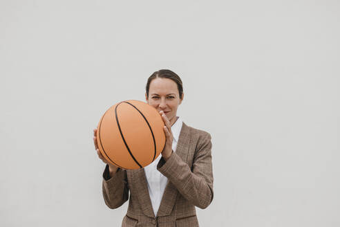Geschäftsfrau hält Basketball, während sie gegen eine weiße Wand steht - DMGF00512