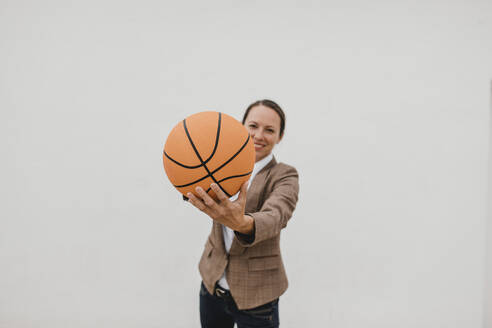 Verspielte weibliche Fachkraft mit Basketball steht gegen eine weiße Wand, während sie Pause macht - DMGF00517