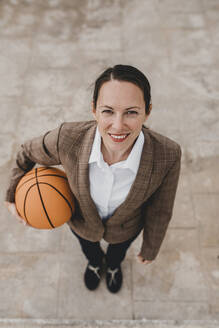 Lächelnde Geschäftsfrau mit Basketball auf dem Fußweg in der Pause - DMGF00519