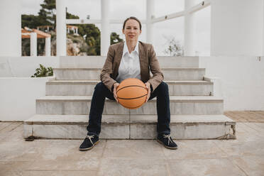 Female entrepreneur with basketball sitting on steps - DMGF00520