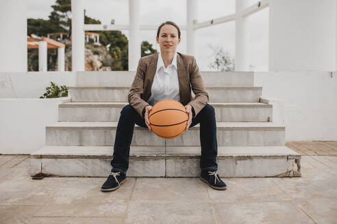 Unternehmerin mit Basketball auf einer Treppe sitzend - DMGF00520