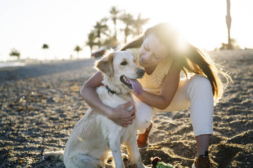 Lächelnde Frau umarmt Hund während auf Sand während sonnigen Tag am Wochenende - MPPF01544