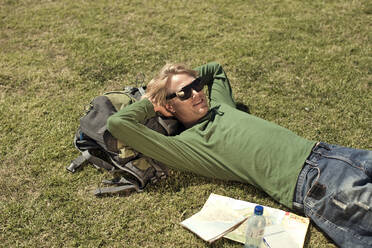 Male tourist lying down on grass in public park during weekend - AJOF01154