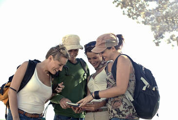 Smiling male and female tourists looking at map while standing against sky - AJOF01159