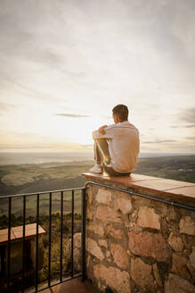 Young man sitting on retaining wall during sunset - ACPF01170