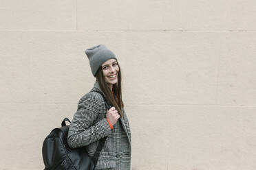 Woman in warm clothing holding backpack against wall - XLGF01245