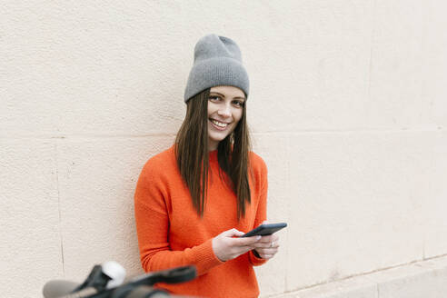 Schöne Frau in warmer Kleidung hält Smartphone gegen die Wand - XLGF01251