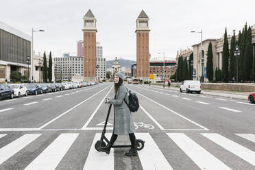Frau mit Elektroroller beim Überqueren der Straße in der Stadt - XLGF01253