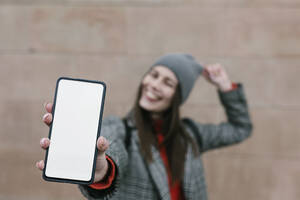 Woman showing blank smart phone screen against wall - XLGF01265