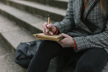 Frau schreibt in ein Buch, während sie auf einer Treppe sitzt - XLGF01271