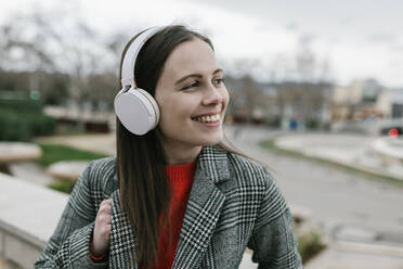 Young woman with headphones while looking away in city - XLGF01276