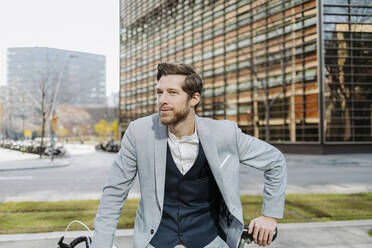 Male professional with bicycle standing in city while looking away - GMCF00024