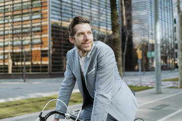 Smiling businessman on bicycle in city - GMCF00027