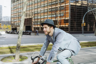 Male professional wearing hat riding bicycle while traveling in city - GMCF00032