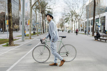 Männlicher Unternehmer zu Fuß mit Fahrrad auf der Straße in der Stadt - GMCF00035