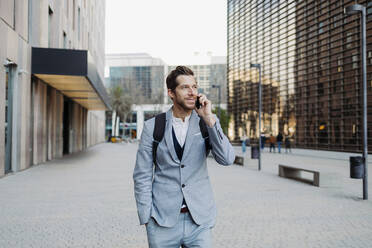 Businessman standing with hand in pocket talking on smart phone - GMCF00040