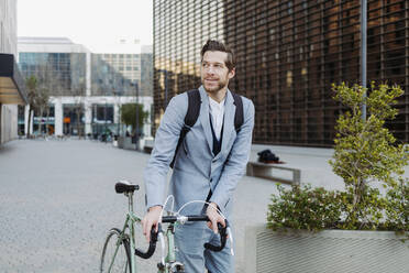 Male commuter wearing back pack walking with bicycle on road in city - GMCF00042