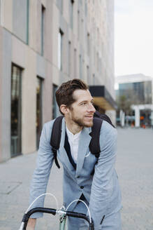 Male professional riding on bicycle in city while looking away - GMCF00043