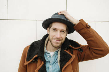 Smiling mid adult man wearing hat against white wall - GMCF00070