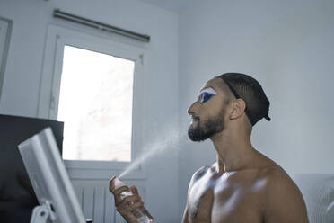Mann ohne Hemd mit Haarnetz, der sein Make-up mit Spray fixiert - RDGF00324
