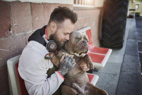 Männlicher Fitnesstrainer umarmt Bulldogge vor dem Fitnessstudio - RORF02617