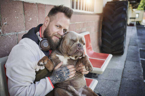 Männlicher Fitnesstrainer umarmt Bulldogge vor dem Fitnessstudio - RORF02619