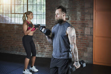 Female and male athlete exercising with dumbbells in gym - RORF02620