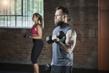 Aktiver weiblicher und männlicher Sportler beim Training mit Hanteln im Fitnessstudio - RORF02622