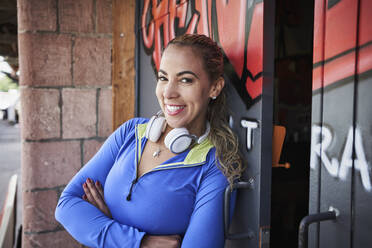 Lächelnder weiblicher Fitnesstrainer, der sich vor dem Fitnessstudio an die Tür lehnt - RORF02628