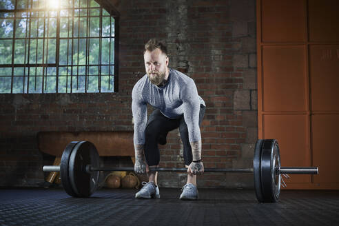 Aktiver männlicher Sportler, der eine Langhantel hebt, während er im Fitnessstudio trainiert - RORF02657