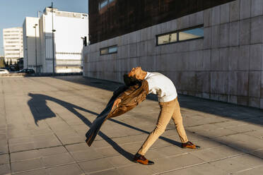 Männlicher Tänzer, der bei Sonnenuntergang auf dem Fußweg vor einem Gebäude tanzt - TCEF01622