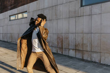 Male dancer enjoying music while dancing against building - TCEF01627