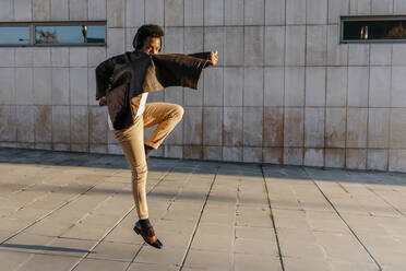 Male dancer wearing headphones while practicing dance against building - TCEF01629