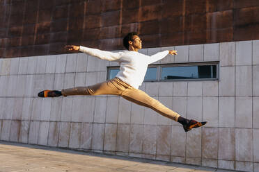 Happy male dancer doing grand jeté against building - TCEF01634