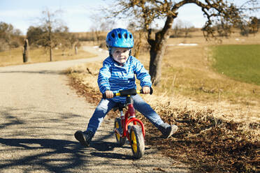 Boy wearing cycling helmet riding balance bike on road during sunny day - SEBF00290