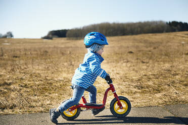 Boy wearing cycling helmet riding balance bike on road - SEBF00291