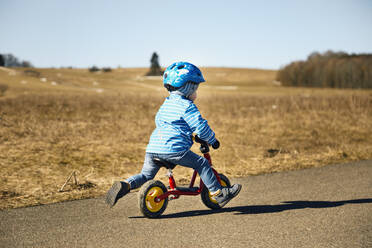 Boy with cycling helmet riding balance bicycle on road - SEBF00292