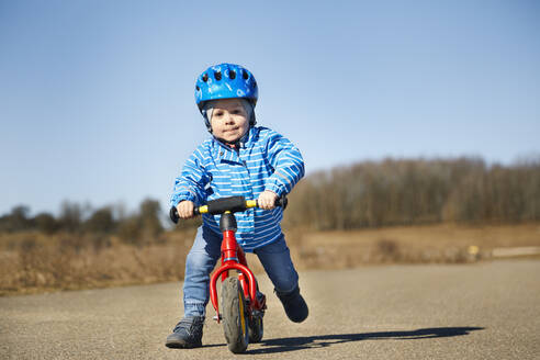 Junge schiebt beim Spielen mit dem Balance-Bike auf der Straße - SEBF00295