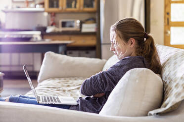Teenager-Mädchen schaut auf Laptop auf Sofa - MINF15840