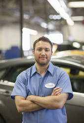 Automechaniker in einer Reparaturwerkstatt, junger weißer Mann in Uniform mit Namensschild - MINF15848