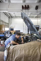 Ein Mechaniker in einer Autowerkstatt lehnt sich in den Motor eines Autos, an dem er gerade arbeitet - MINF15855