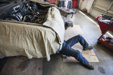 Mechaniker liegt auf einem Wagen unter einem Auto in einer Autowerkstatt - MINF15862