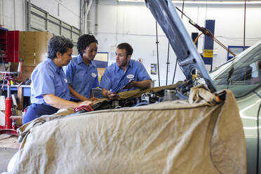 Drei Mechaniker teilen sich ein digitales Tablet und planen die Arbeit an einem Auto, das zur Reparatur ansteht - MINF15871