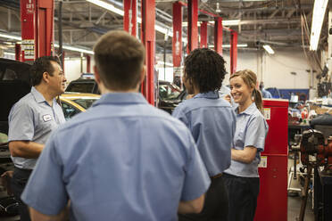 Ein Team von Mechanikern, die an einem Auto arbeiten, diskutiert ein Problem in einer Autowerkstatt - MINF15882