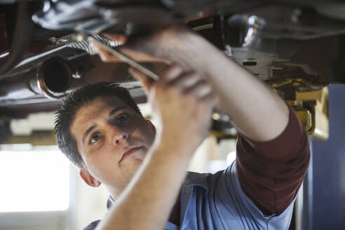 Mechaniker in einer Werkstatt arbeitet an der Unterseite eines Autos auf einer Hebebühne - MINF15885